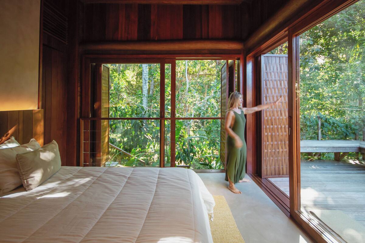 A bedroom with a large bed, a view of the outdoors through a sliding door, and a wooden deck outside.