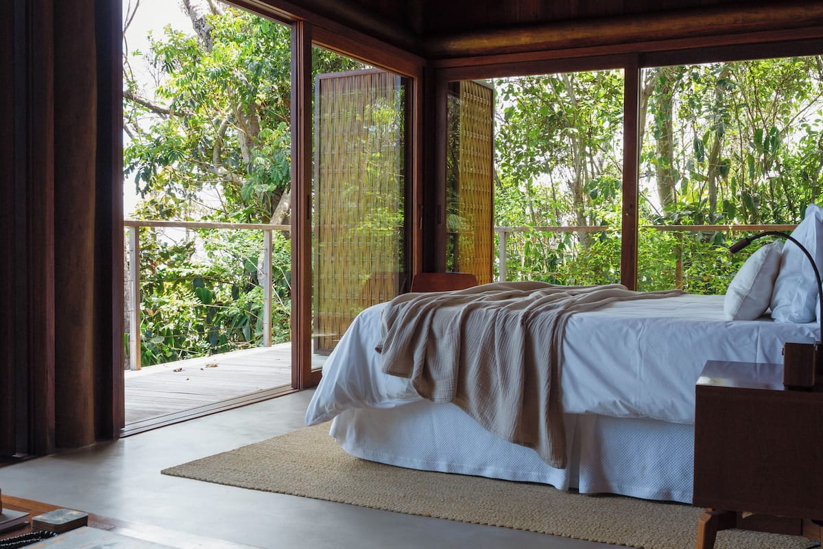 A bedroom with a large bed, wooden walls, and a view of lush greenery outside.
