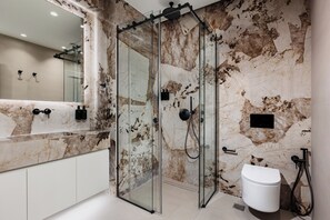 Ein modernes Badezimmer mit einer Duschkabine aus Glas, einer Marmorwand, einem großen Spiegel und einer weißen Toilette.