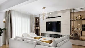 A modern living room with a large sofa, a flat-screen TV mounted on the wall, and a decorative chandelier. - 4bd Ensuite Luxury Residence Kolonaki, Apartment (Athens)