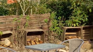 Un patio al aire libre con una mesa redonda de metal y dos sillas de metal, rodeado de rocas y una cerca de madera.