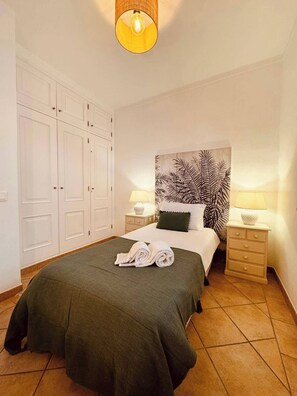 A neatly arranged bedroom with a bed, two bedside tables with lamps, a large wardrobe, and a wall with a leaf pattern.
