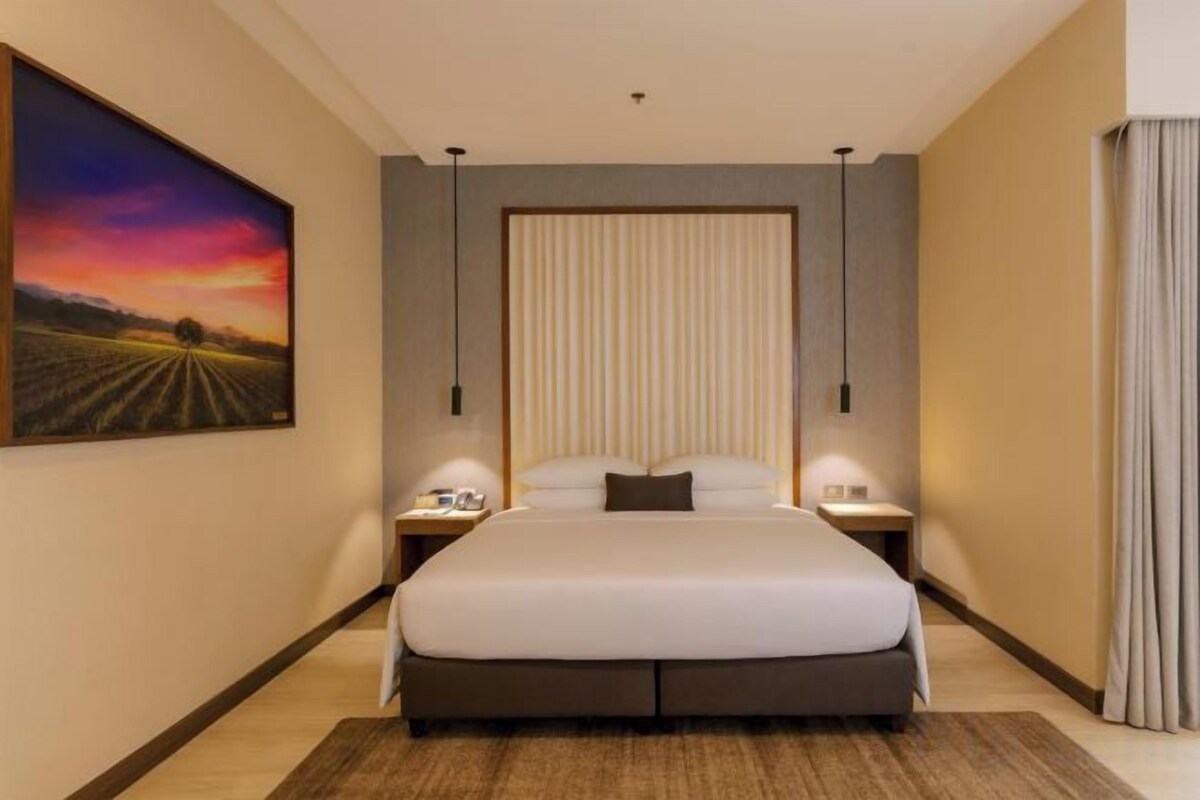 Una camera d'albergo con un letto grande, comodini, un quadro appeso e una finestra con tende.