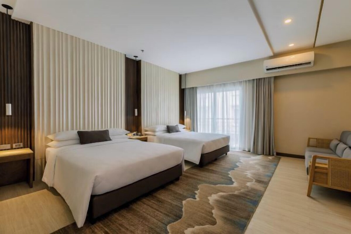Habitación de hotel con dos camas, un sofá y un ventanal con cortinas.