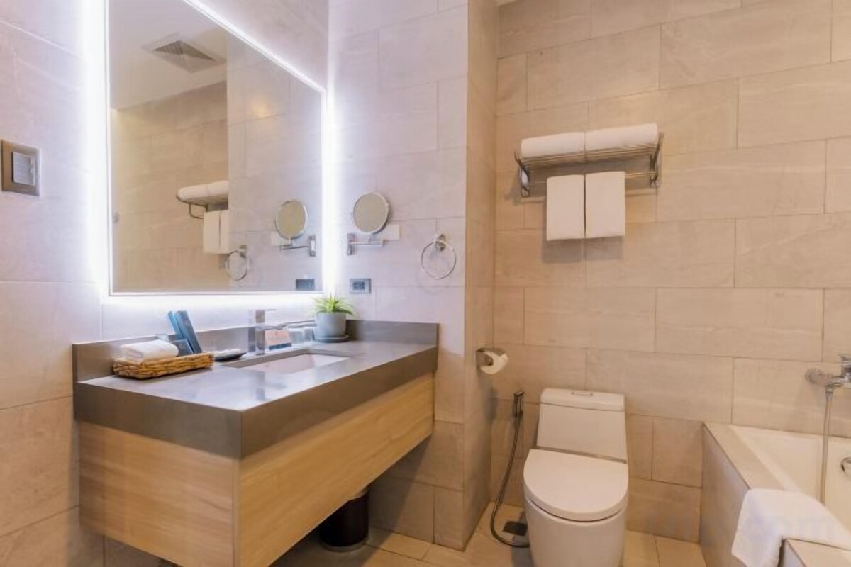 Un baño moderno con tocador de madera, un espejo grande, inodoro y zona de ducha.