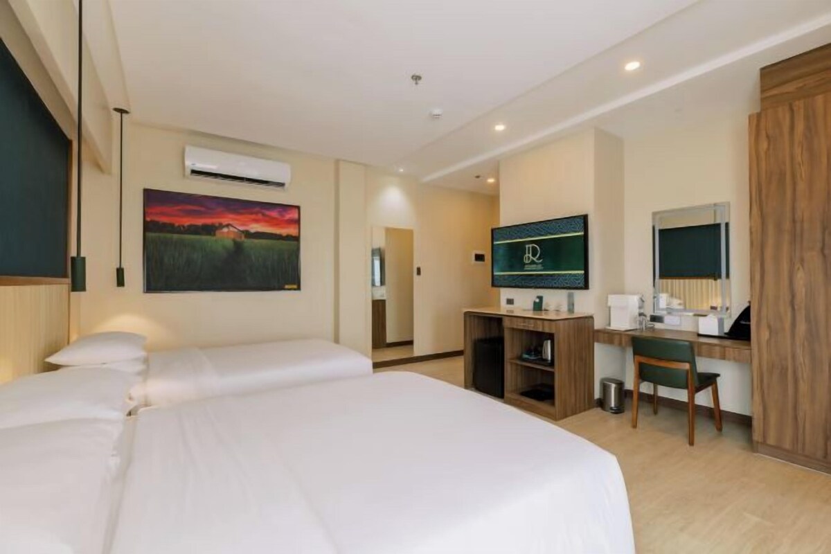 A hotel room with a large bed, a desk with a computer, a TV, and a painting of a sunset.