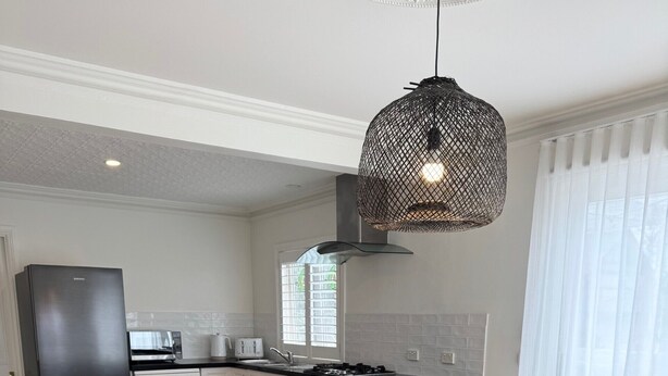Une cuisine moderne avec un réfrigérateur noir, un four à micro-ondes et une cuisinière. On y trouve une table à manger avec des chaises blanches et un luminaire suspendu.