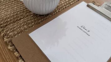 A white vase with flowers on a woven placemat, a clipboard with a welcome note, and a wooden table.