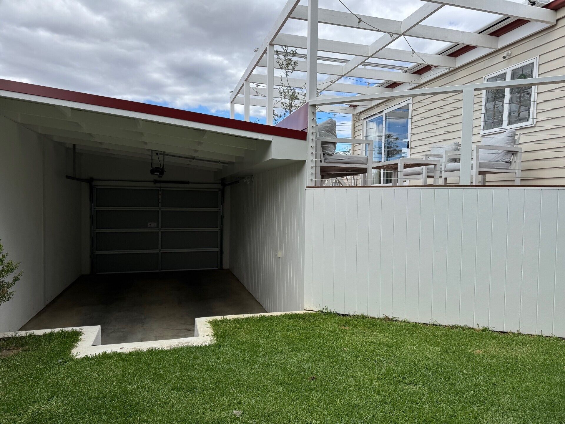 A garage with a covered entrance, a white fence, and a grassy yard.
