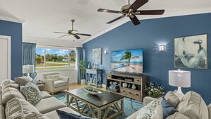 Ein Wohnzimmer mit großem Fernseher, zwei Deckenventilatoren, einem Couchtisch und einem Sofa.