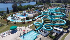 Ein Wasserpark mit großem Pool, mehreren Rutschen und einer Liegefläche mit Liegestühlen und Sonnenschirmen.