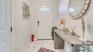 A hallway with a white door, a decorative mirror, a small plant, and a fire extinguisher. - Stylish home close to golf court & a casino (Tulsa)
