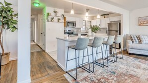 A modern kitchen with white cabinets, a central island with bar stools, and pendant lighting. - Stylish home close to golf court & a casino (Tulsa)