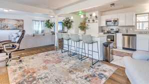 A modern kitchen with white cabinets, stainless steel appliances, and a bar area with stools. - Stylish home close to golf court & a casino (Tulsa)