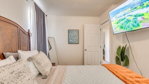 A bedroom with a bed, a television mounted on the wall, and a door leading to another room. - Stylish home close to golf court & a casino (Tulsa)