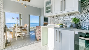 A modern kitchen with a view of the sea, featuring white cabinets, patterned backsplash, and a dining area with a view. - Dihangfa - sleeps 6 guests  in 3 bedrooms (Nefyn)