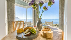 A table with cheese, grapes, and a candle, overlooking a beach with a clear view of the ocean. - Dihangfa - sleeps 6 guests  in 3 bedrooms (Nefyn)