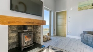 A modern living room with a stone fireplace, a flat-screen TV mounted above it, and a view of the sea through a glass door. - Dihangfa - sleeps 6 guests  in 3 bedrooms (Nefyn)