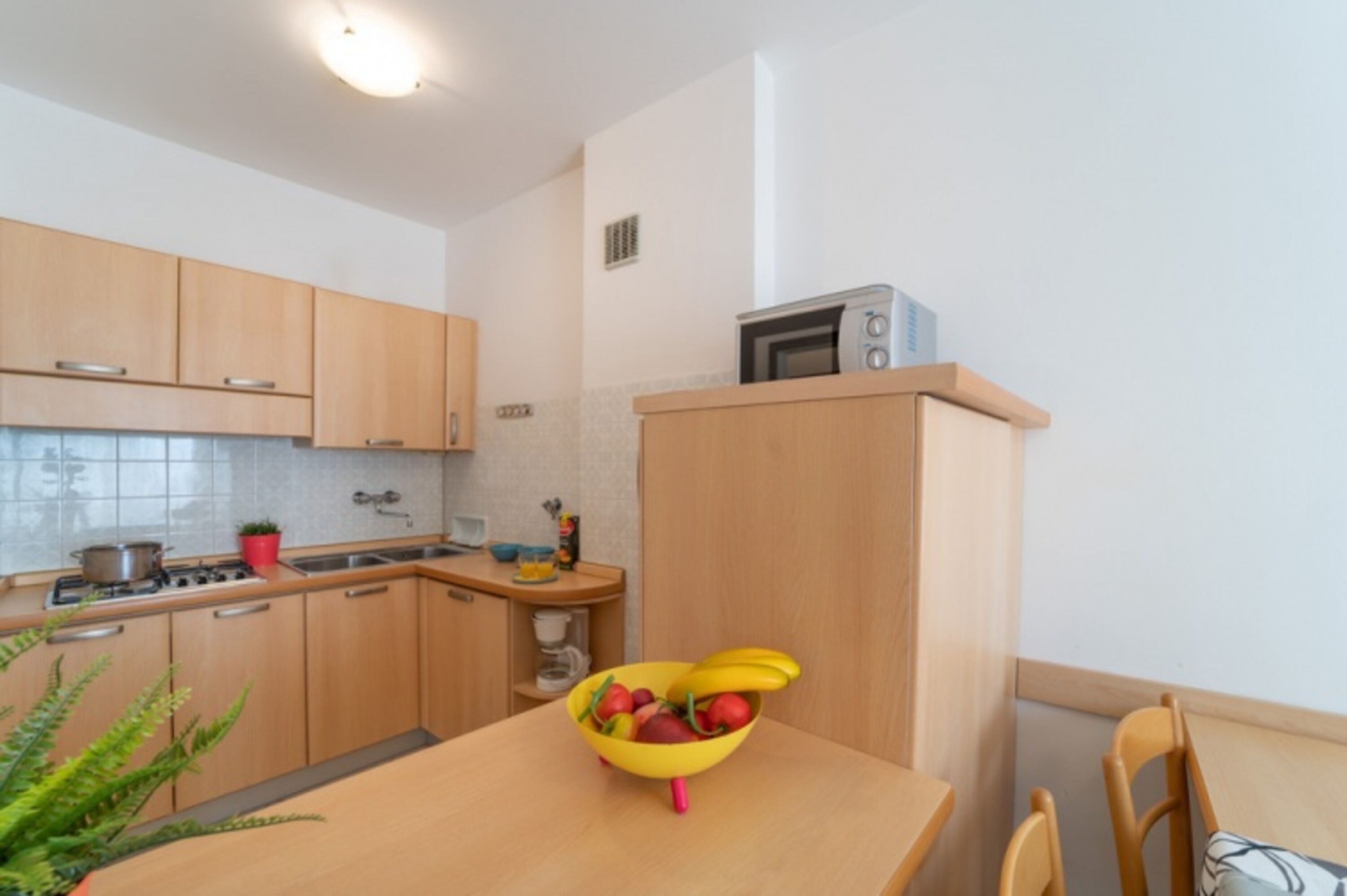 Una cocina con armarios de madera, microondas, estufa y un tazón de fruta en la mesa.