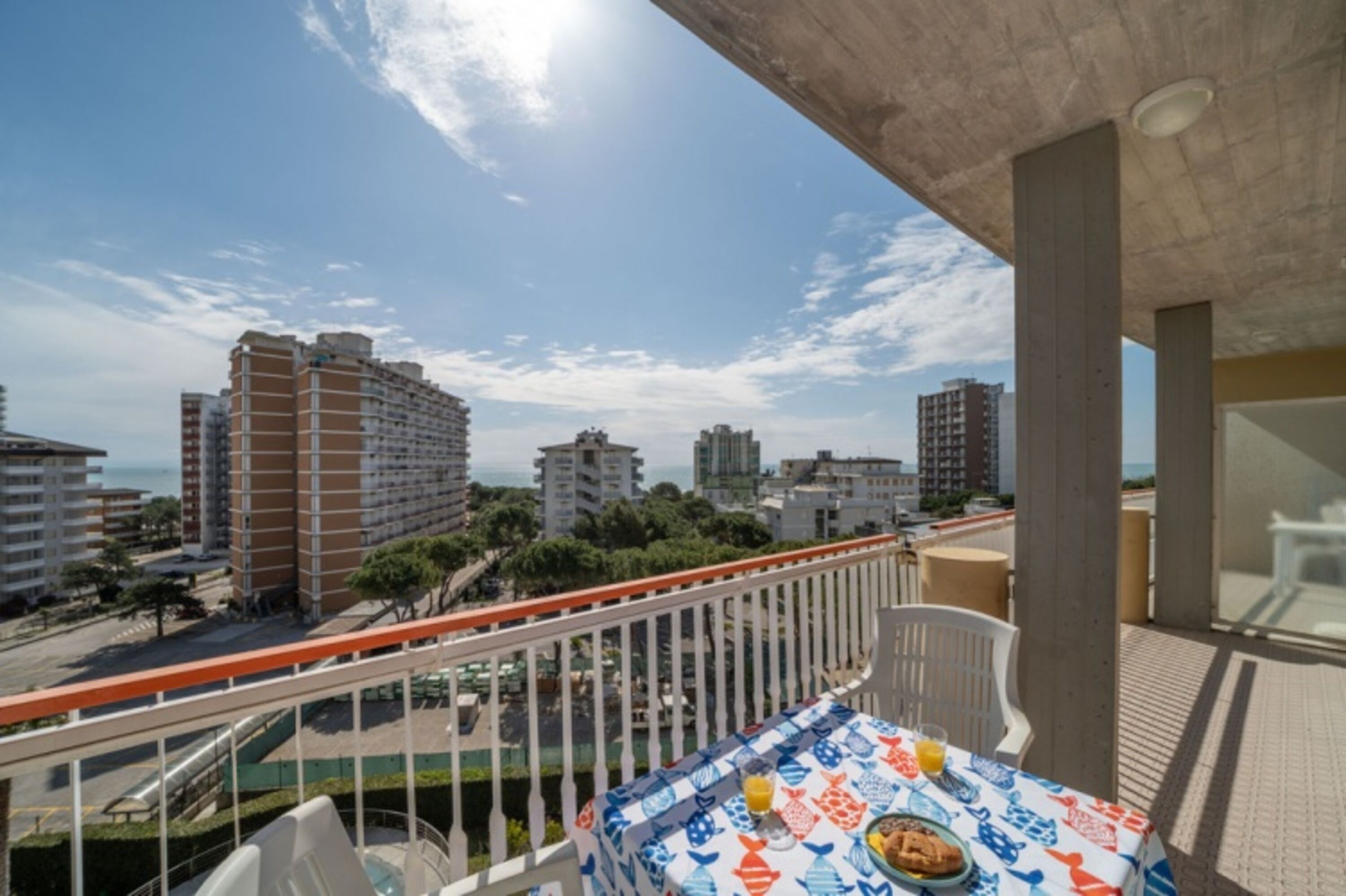 Varanda com mesa posta para refeições, com vista para paisagem urbana com edifícios altos e céu claro.