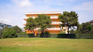 A multi-story residential building with a flat roof and a uniform orange facade. - Perfectly located flat (Bibione)