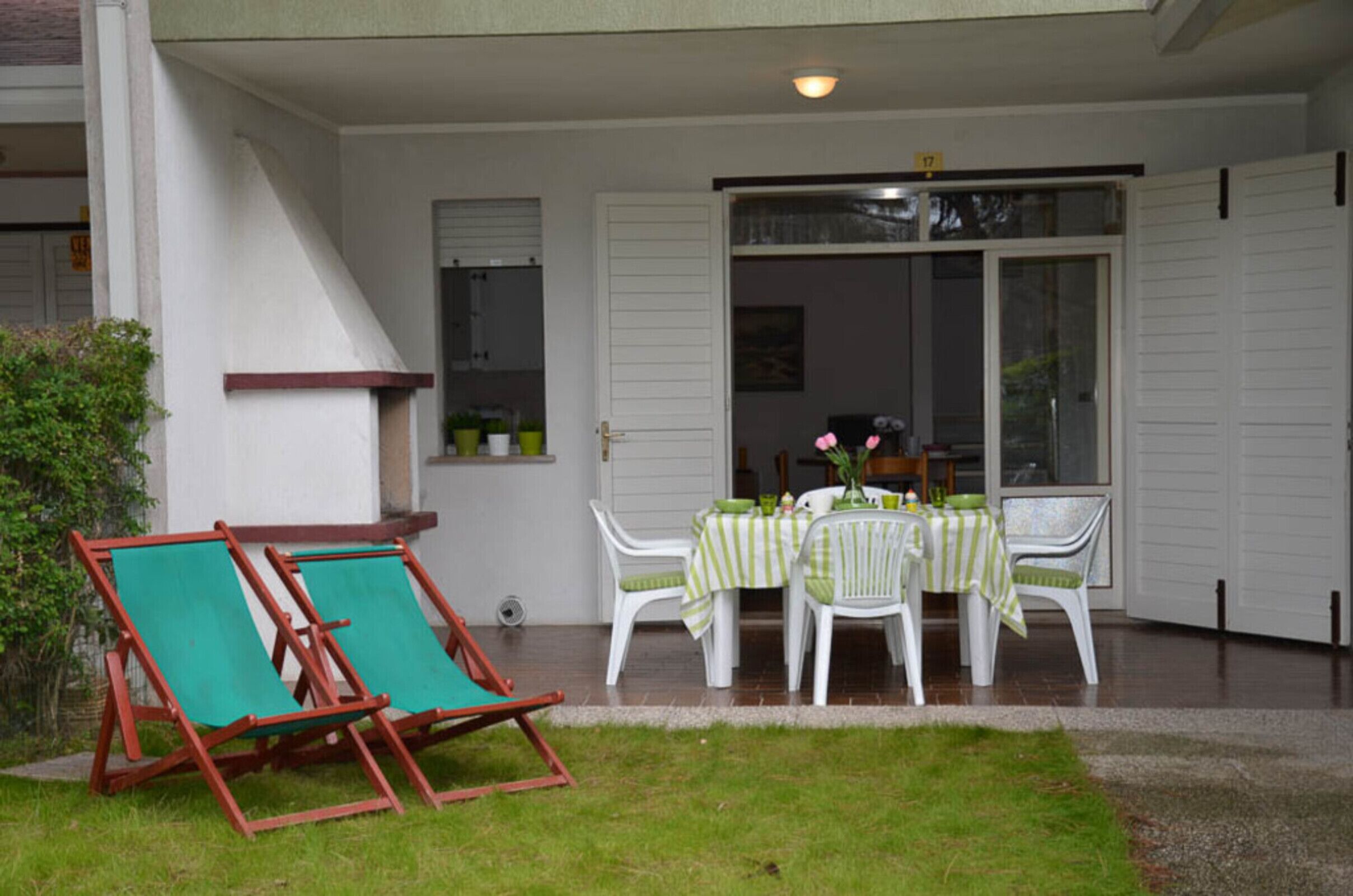 Un patio con una mesa preparada para dos, dos sillones de relax y un ventanal corredero que da a una habitación.