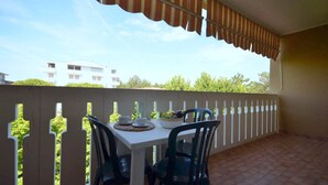 Een balkon met een witte tafel en stoelen, een gestreept zonnescherm en uitzicht op gebouwen en bomen.