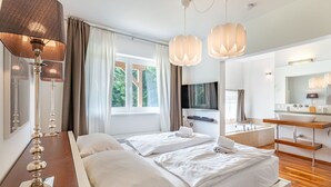 A modern hotel room with a bed, bedside table, lamp, TV, and a bathroom with a sink and mirror. - Beautiful apartment for 6 people with WIFI, TV, terrace and pets allowed (Frauenstein)