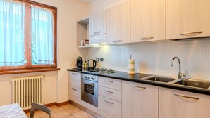 A compact kitchen with light wood cabinets, a black countertop, a built-in oven, a sink, and a window with curtains. - Cosy apartment for 2 guests with WIFI, TV and balcony (Dongo)