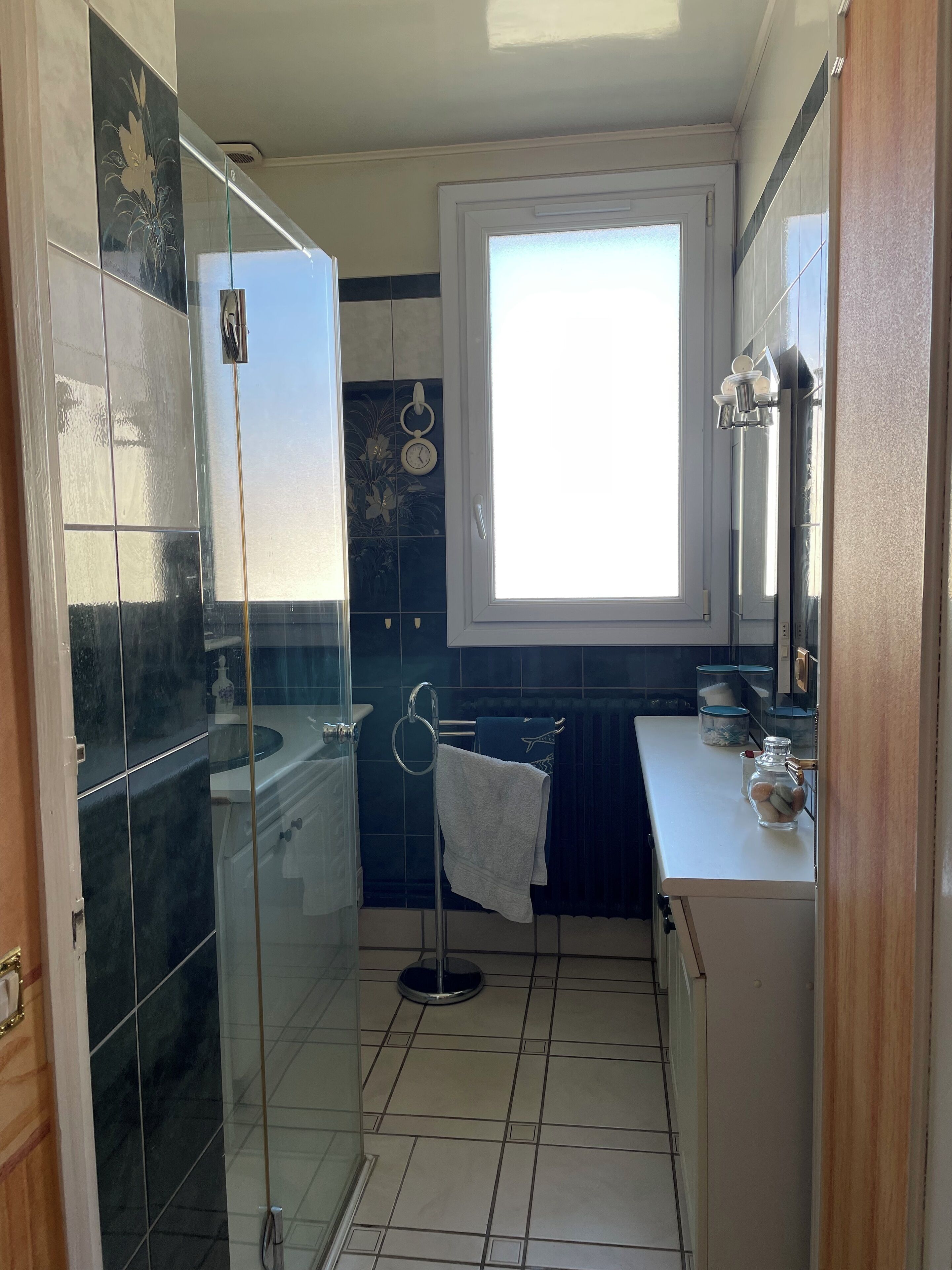 A bathroom with a glass shower enclosure, a window, a sink, and a mirror.