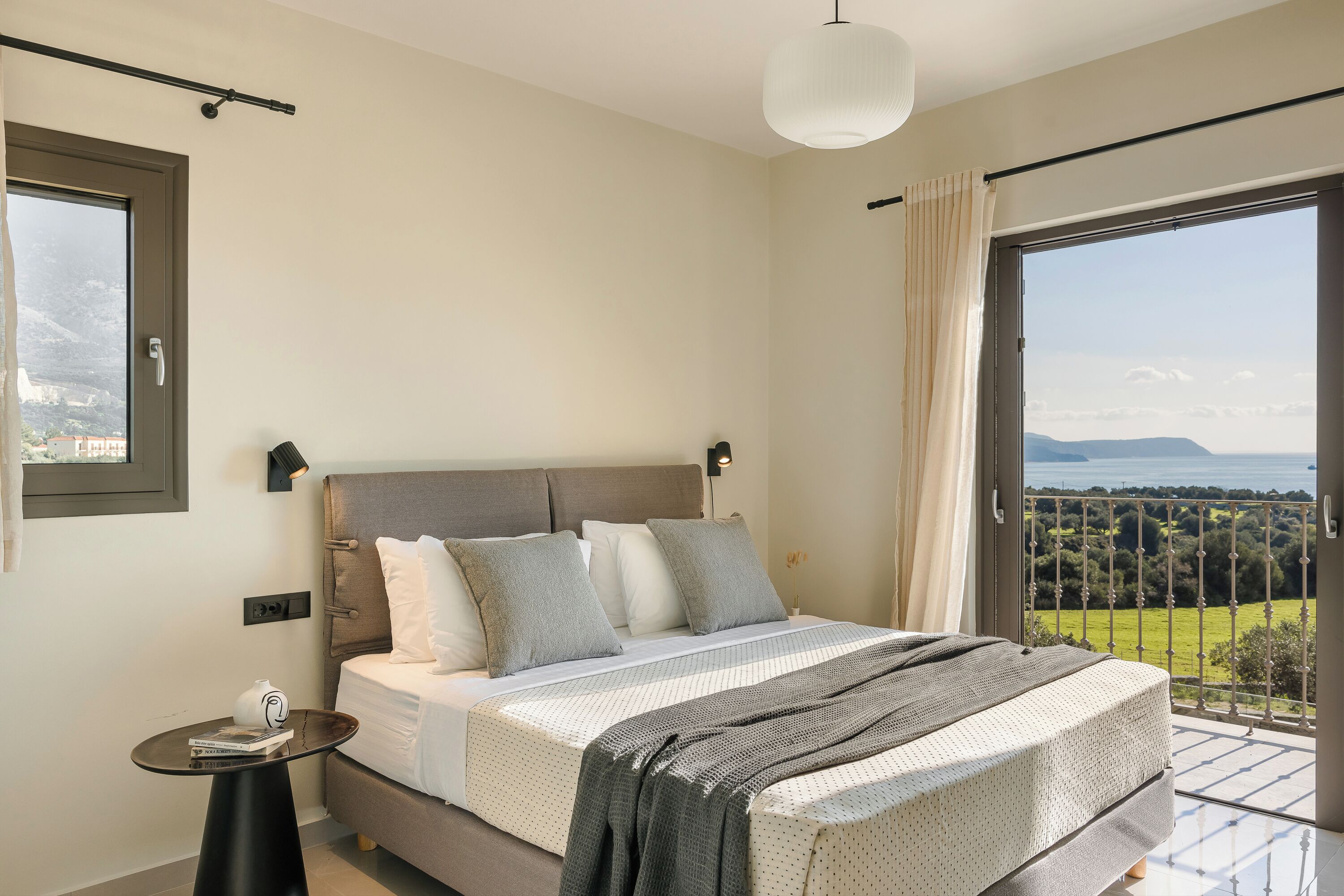 A bedroom with a large bed, a small table, and a balcony with a view.