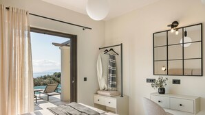 A bedroom with a bed, a chair, a bedside table, a hanging towel, a mirror, and a view of the outdoors.