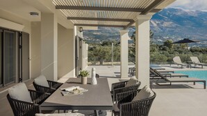 A covered outdoor seating area with a pool and mountain views.