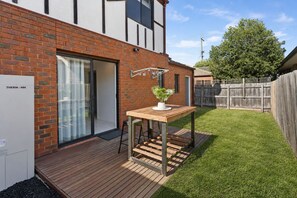 A modern house with a brick exterior, a wooden deck, and a sliding glass door leading to a patio.