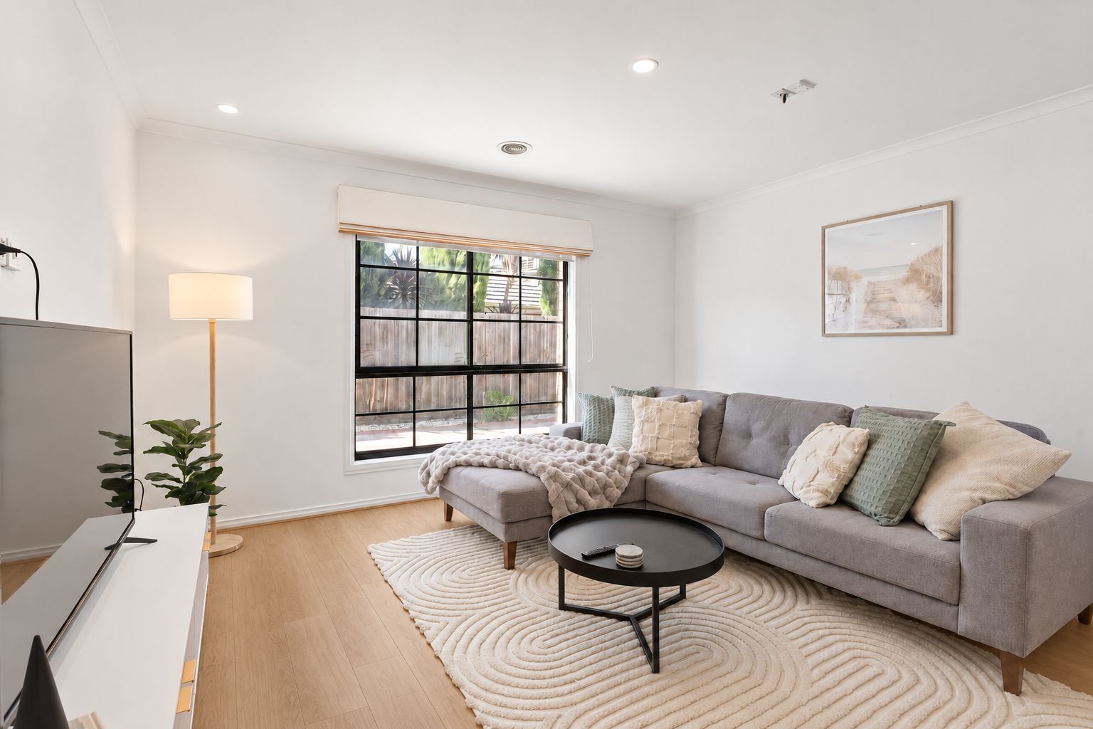 A modern living room with a grey sofa, a round coffee table, and a large window with a view of greenery.