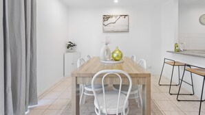 A dining area with a wooden table, white chairs, and a painting on the wall.