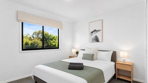 A neatly arranged bedroom with a bed, bedside tables, a window with a view, and a framed picture on the wall.