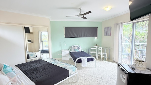 A bedroom with a bed, a desk, a chair, a ceiling fan, and a window.