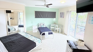 A bedroom with a bed, a desk, a chair, a ceiling fan, and a window with a view of the outdoors.
