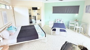 A bedroom with two beds, a desk, a chair, a ceiling fan, and a small potted plant.