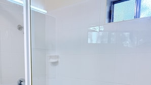 A modern bathroom with white tiles, a glass shower enclosure, and a window with frosted glass.