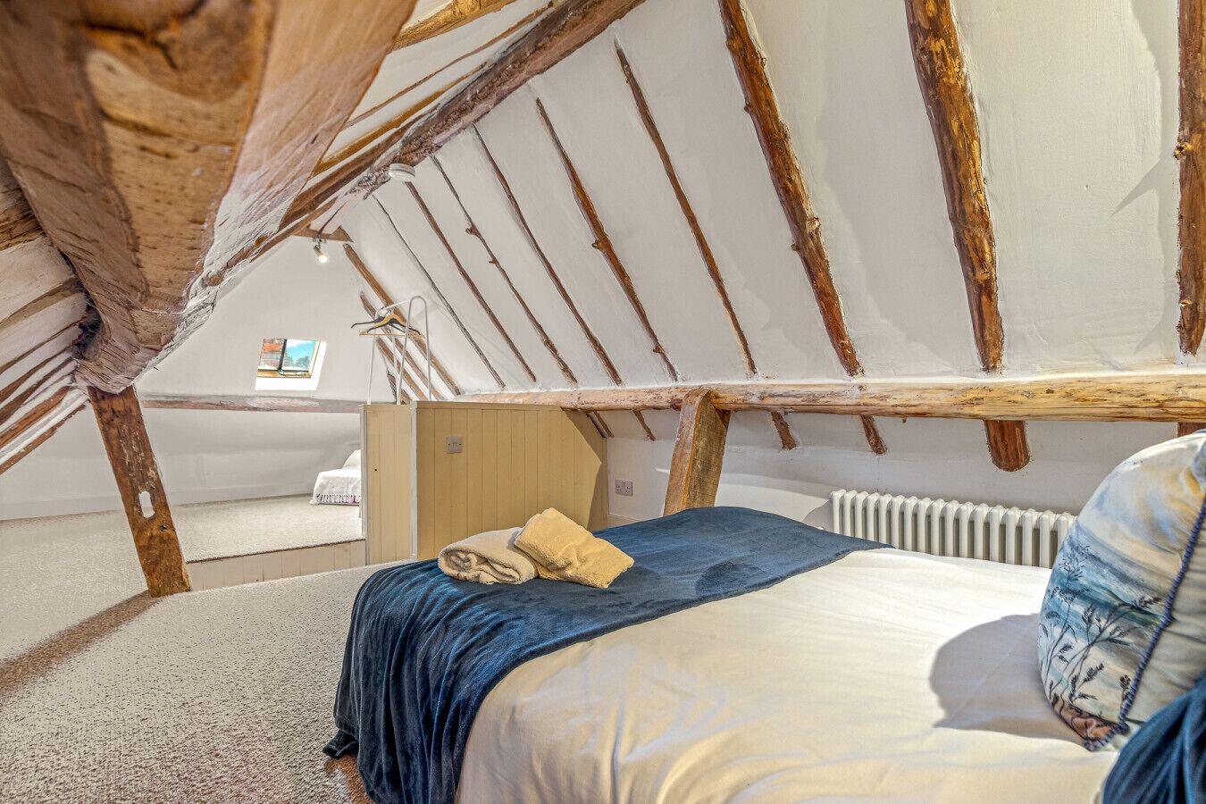 Una camera da letto mansardata accogliente, con travi a vista in legno, un letto con copripiumino blu e beige e un termosifone.