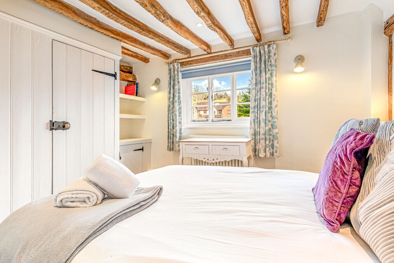 Un dormitorio con una cama grande, techo de madera, ventana con cortinas, mesita de noche y armario.