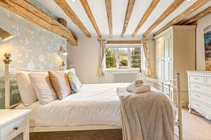 A bedroom with a large bed, a dresser, a radiator, and a window with curtains.