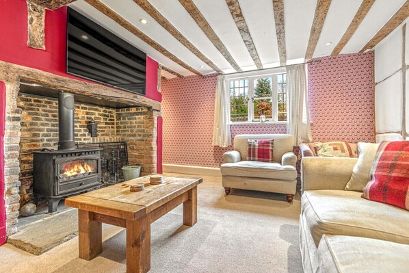 A cozy living room with a brick fireplace, a wooden coffee table, a sofa, and a patterned wallpaper. - Hunts cottage - Pet friendly (Harpsden)