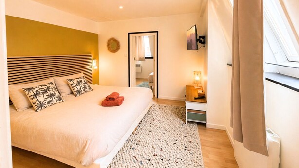 A bedroom with a bed, a bedside table, a lamp, a mirror, and a window with curtains. - Apart'Moment EN GROUPE - Le Cocon du Haut-Pont (Saint-Omer)