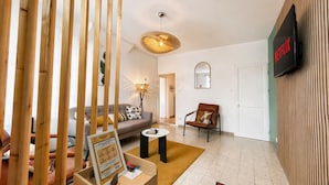 A modern living room with a sofa, a chair, a coffee table, a wall-mounted TV, and a wooden partition. - Apart'Moment EN GROUPE - Le Cocon du Haut-Pont (Saint-Omer)