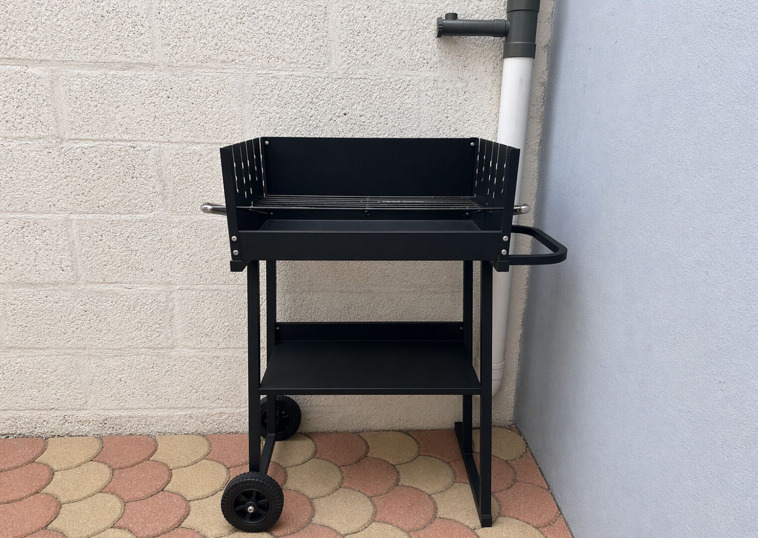 A black metal cart with wheels, positioned against a wall with a white textured surface and a tiled floor.