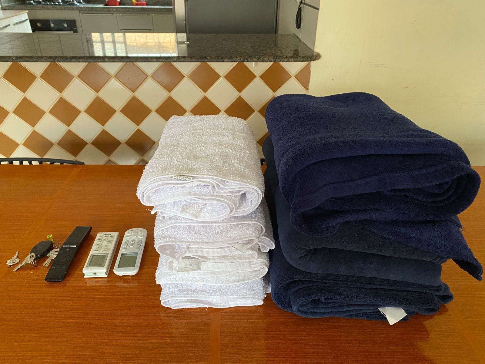 A table with folded towels, keys, and remote controls.