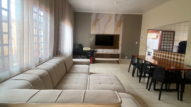 A spacious living room with a large beige sectional sofa, a dining area with a wooden table and chairs, and a flat-screen TV mounted on the wall. - Cozy 3/4 House - Air conditioning in 3/4. Garage. (Palmas)